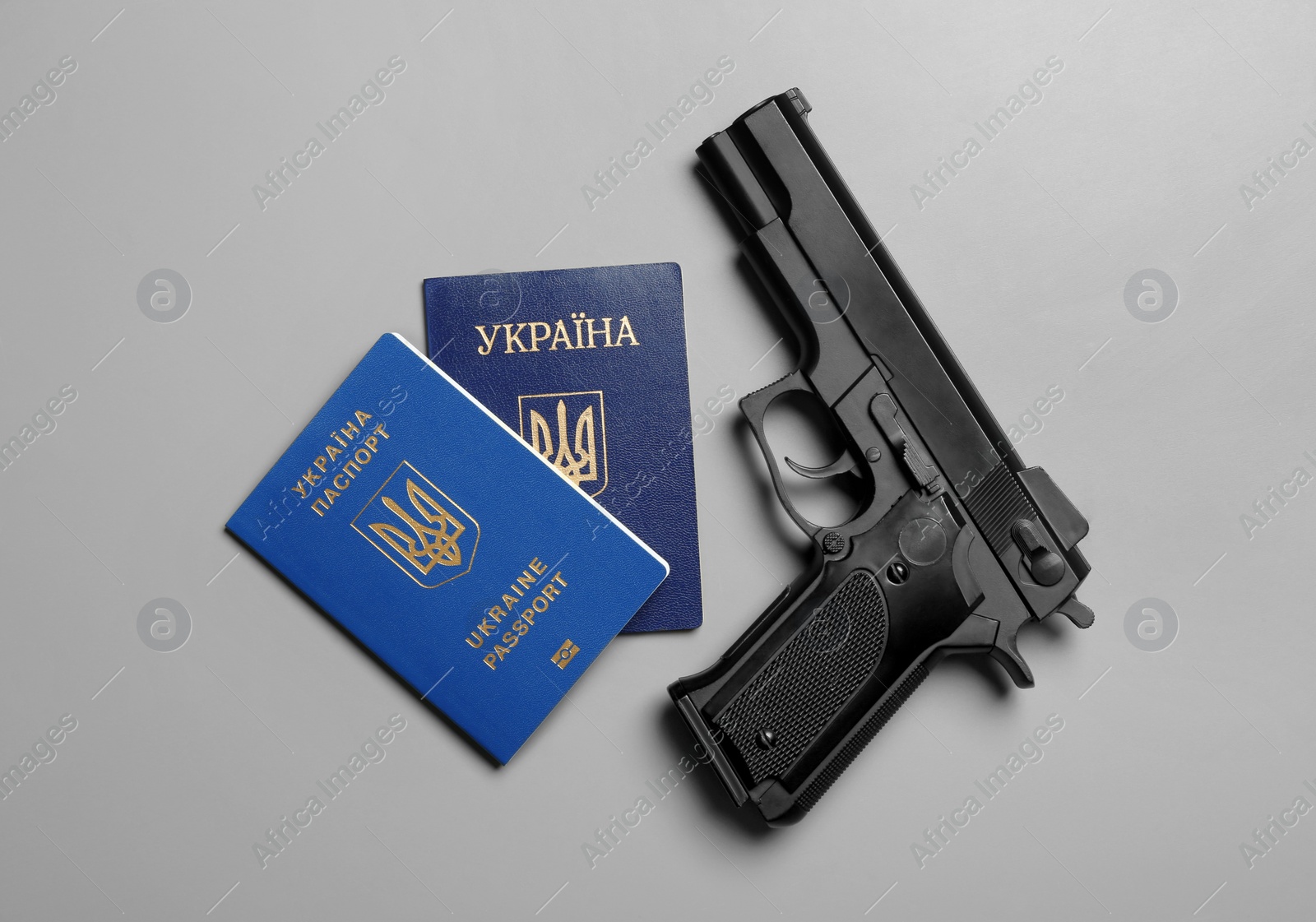 Photo of Gun with Ukrainian passports on grey background, flat lay