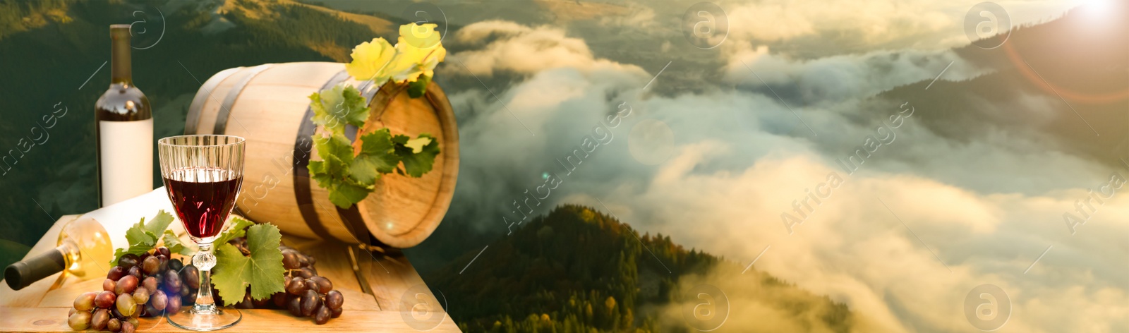 Image of Tasty wine, grapes and barrel on wooden table against beautiful mountain landscape, space for text. Banner design