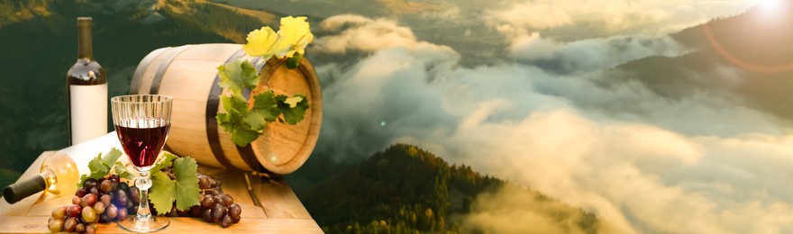 Tasty wine, grapes and barrel on wooden table against beautiful mountain landscape, space for text. Banner design