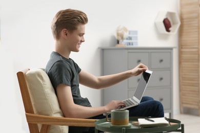 Online learning. Teenage boy with laptop in armchair at home