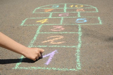 Photo of Child drawing hopscotch with colorful chalk on asphalt outdoors, closeup
