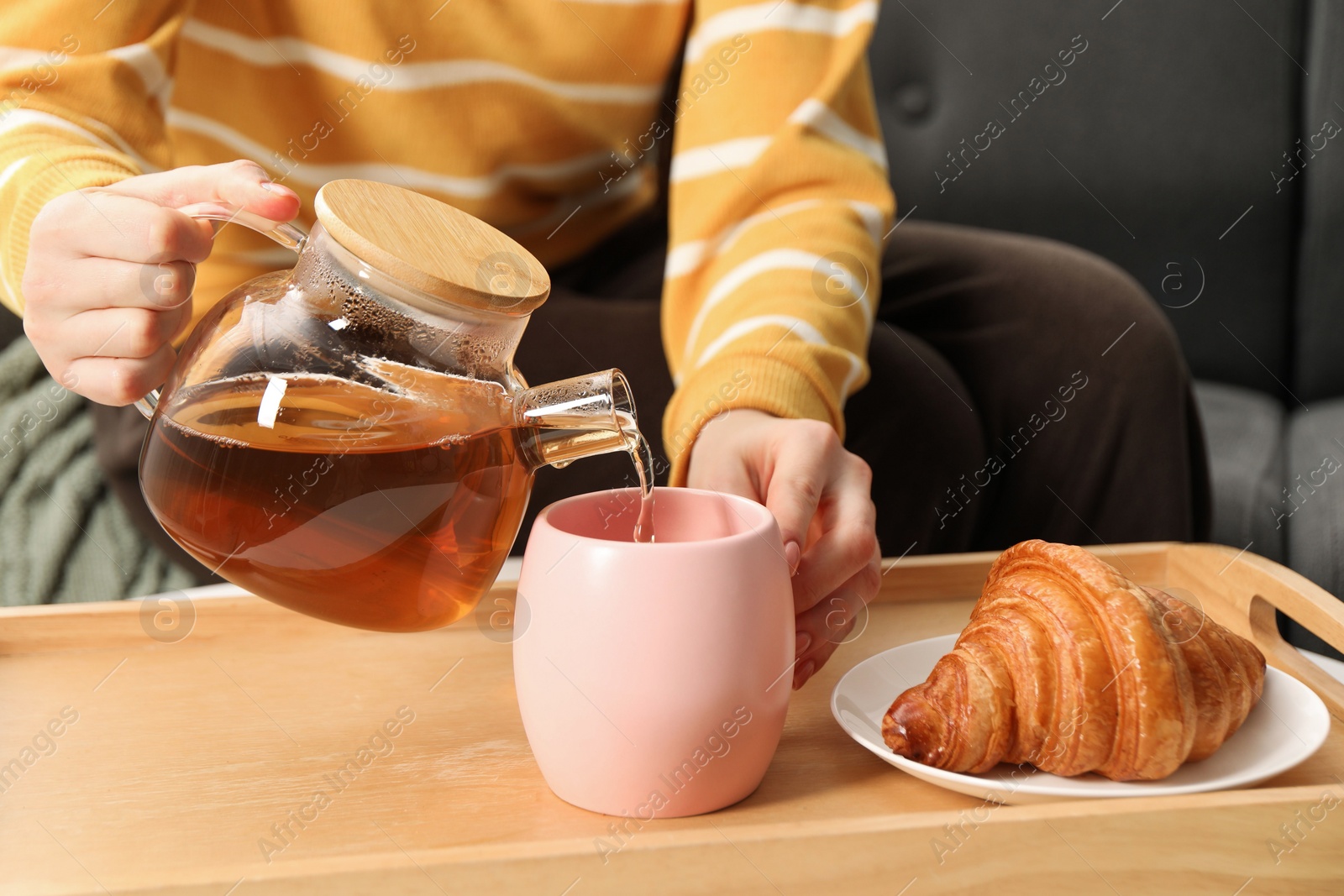 Photo of Woman pouring aromatic tea into cup at table, closeup