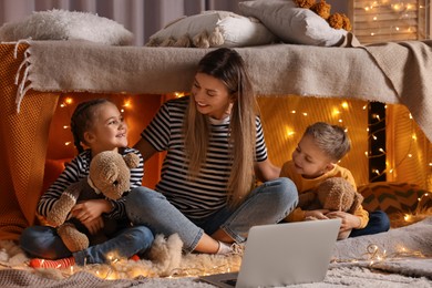 Photo of Mother and her children with laptop in play tent at home