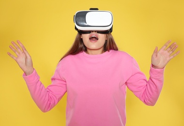 Emotional young woman playing video games with virtual reality headset on color background