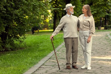 Photo of Senior man with walking cane and mature woman in park. Space for text