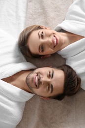 Photo of Happy young couple wearing bathrobes, top view. Visit to spa salon