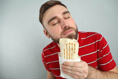Young man with delicious shawarma on grey background, space for text