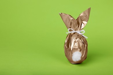 Photo of Easter bunny made of shiny gold paper and egg on green background. Space for text