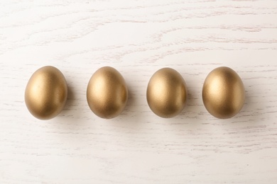 Four golden eggs on wooden background, top view