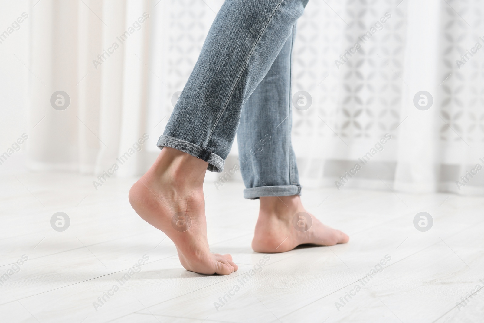 Photo of Barefoot woman walking on white parquet at home, closeup. Heated floor