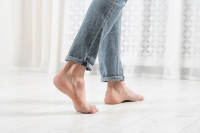 Barefoot woman walking on white parquet at home, closeup. Heated floor