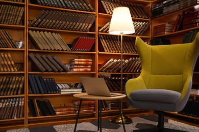 Photo of Cozy home library interior with comfortable armchair, laptop and collectionvintage books on shelves