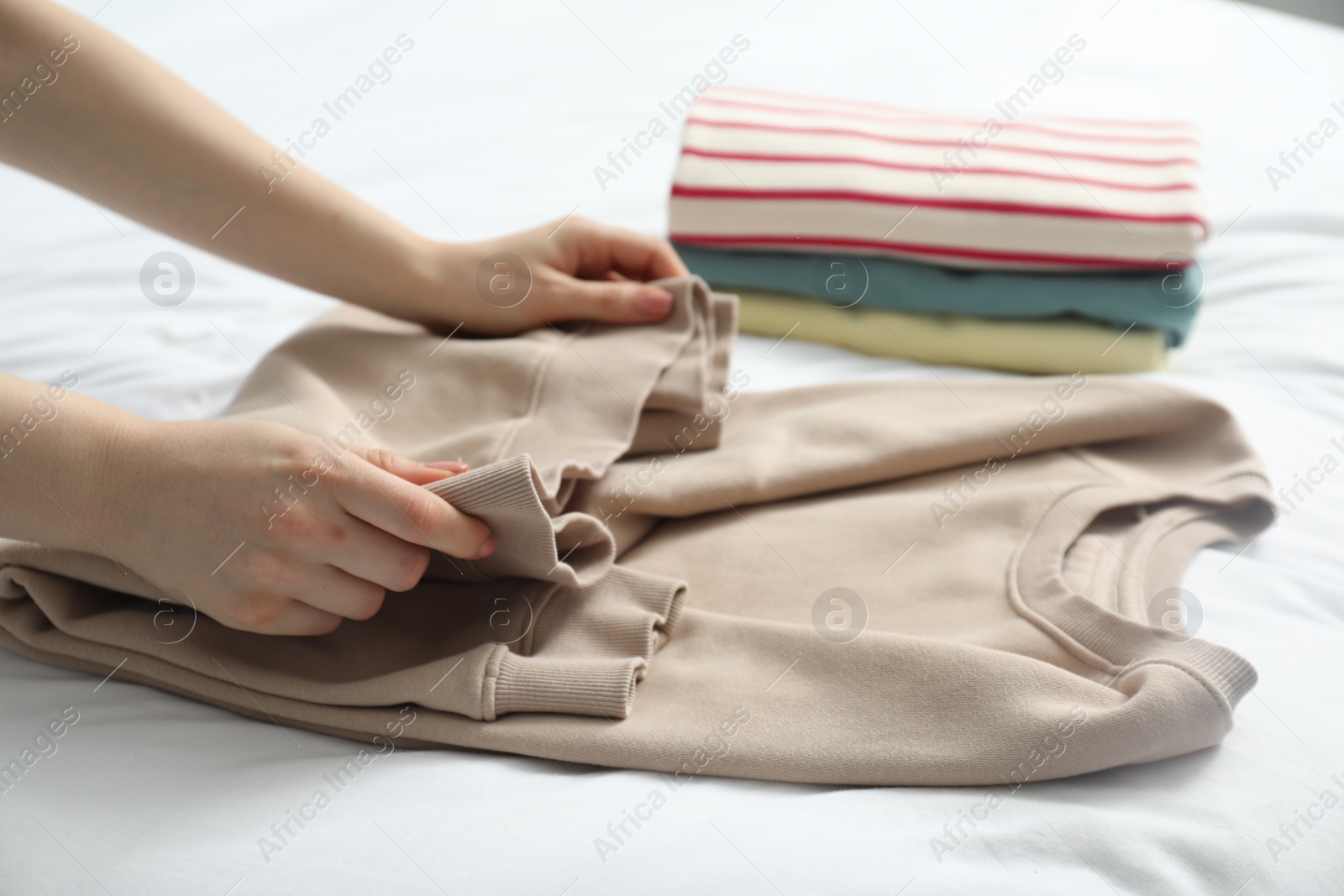 Photo of Woman folding clothes on bed, closeup view