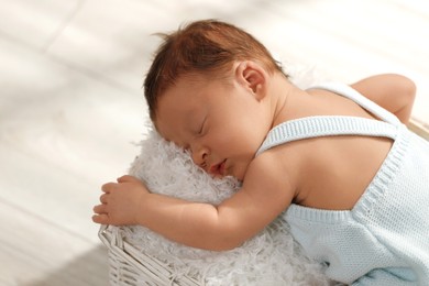 Photo of Cute newborn baby sleeping in white wicker basket indoors, closeup