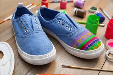 Photo of Light blue sneakers and painting supplies on wooden table, closeup. Customized shoes
