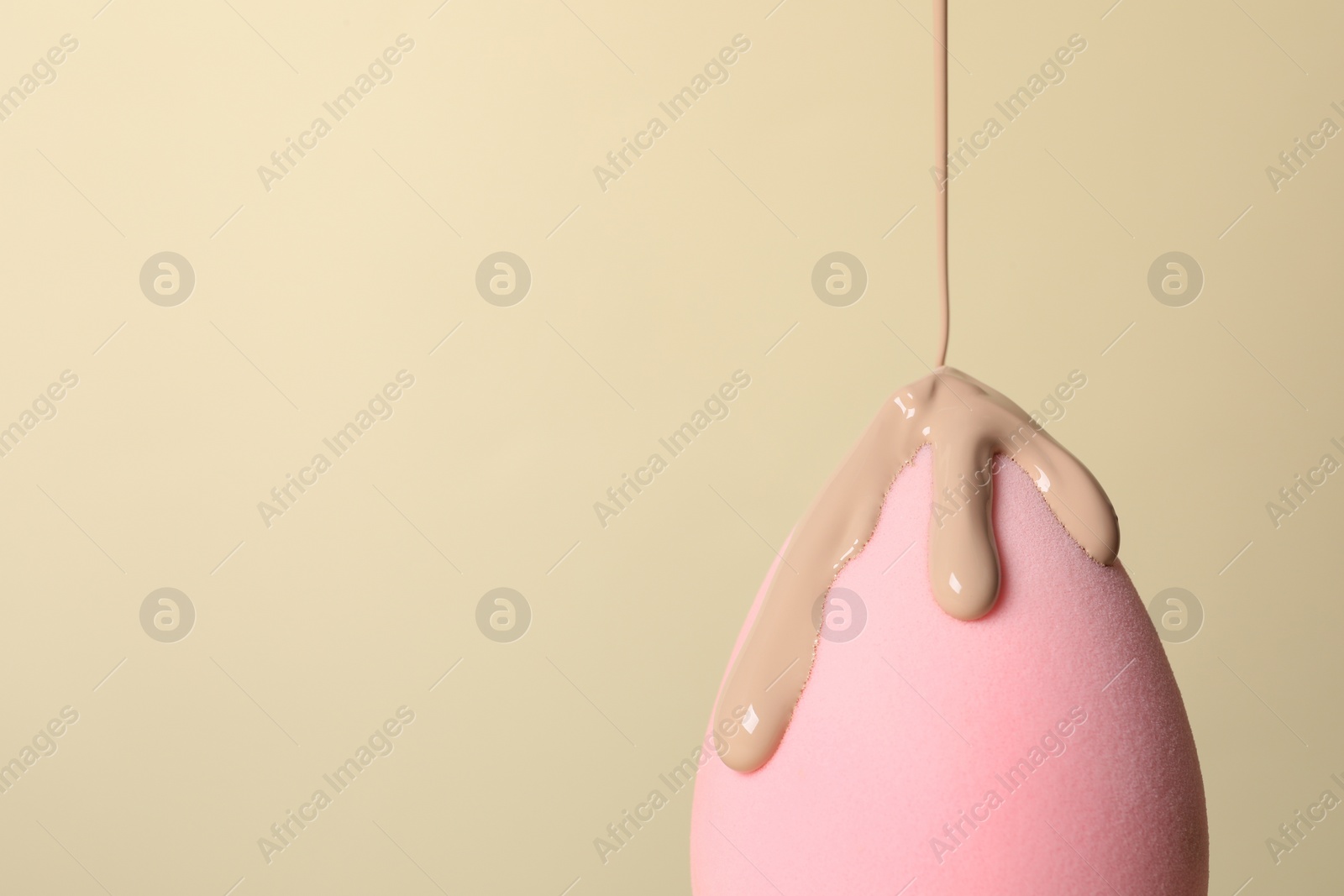 Photo of Skin foundation pouring onto makeup sponge on beige background, space for text