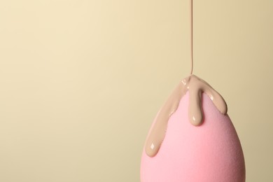 Photo of Skin foundation pouring onto makeup sponge on beige background, space for text