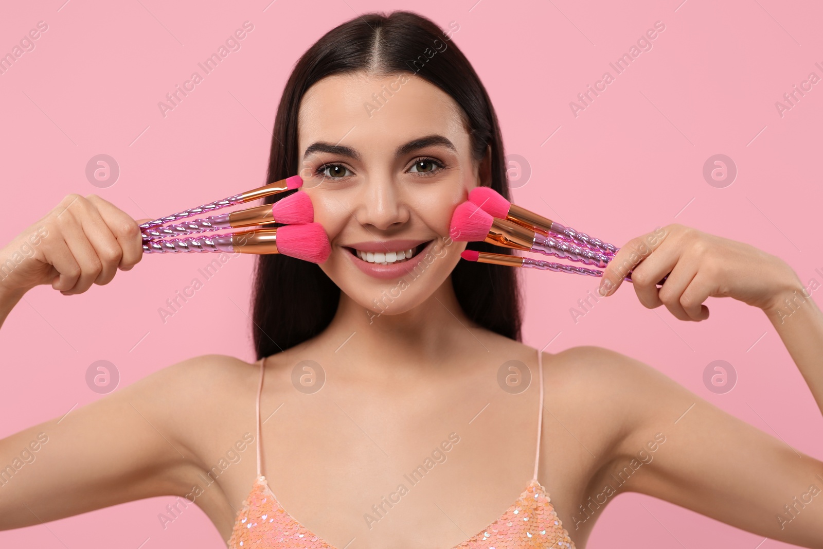 Photo of Happy woman with different makeup brushes on pink background