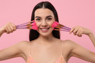 Happy woman with different makeup brushes on pink background