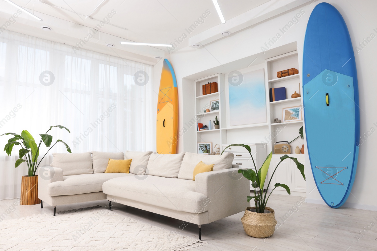 Photo of SUP boards, shelving unit with different decor elements and stylish sofa in room. Interior design