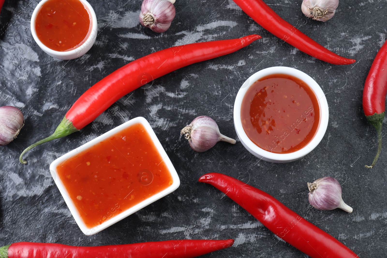 Photo of Spicy chili sauce, peppers and garlic on black textured table, flat lay