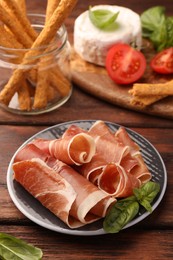 Photo of Rolled slices of delicious jamon and basil on wooden table