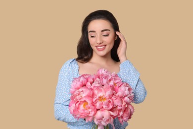 Beautiful young woman with bouquet of pink peonies on beige background