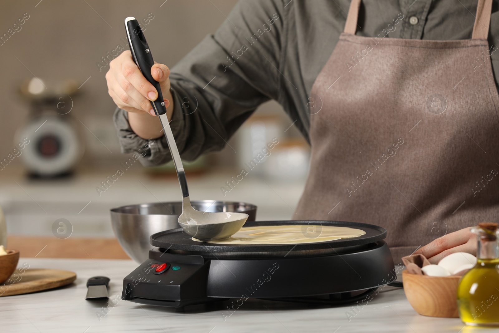 Photo of Woman cooking delicious crepe on electric pancake maker at white marble table in kitchen, closeup