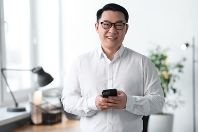 Photo of Portrait of smiling businessman with smartphone in office