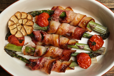 Oven baked asparagus wrapped with bacon in ceramic dish, top view