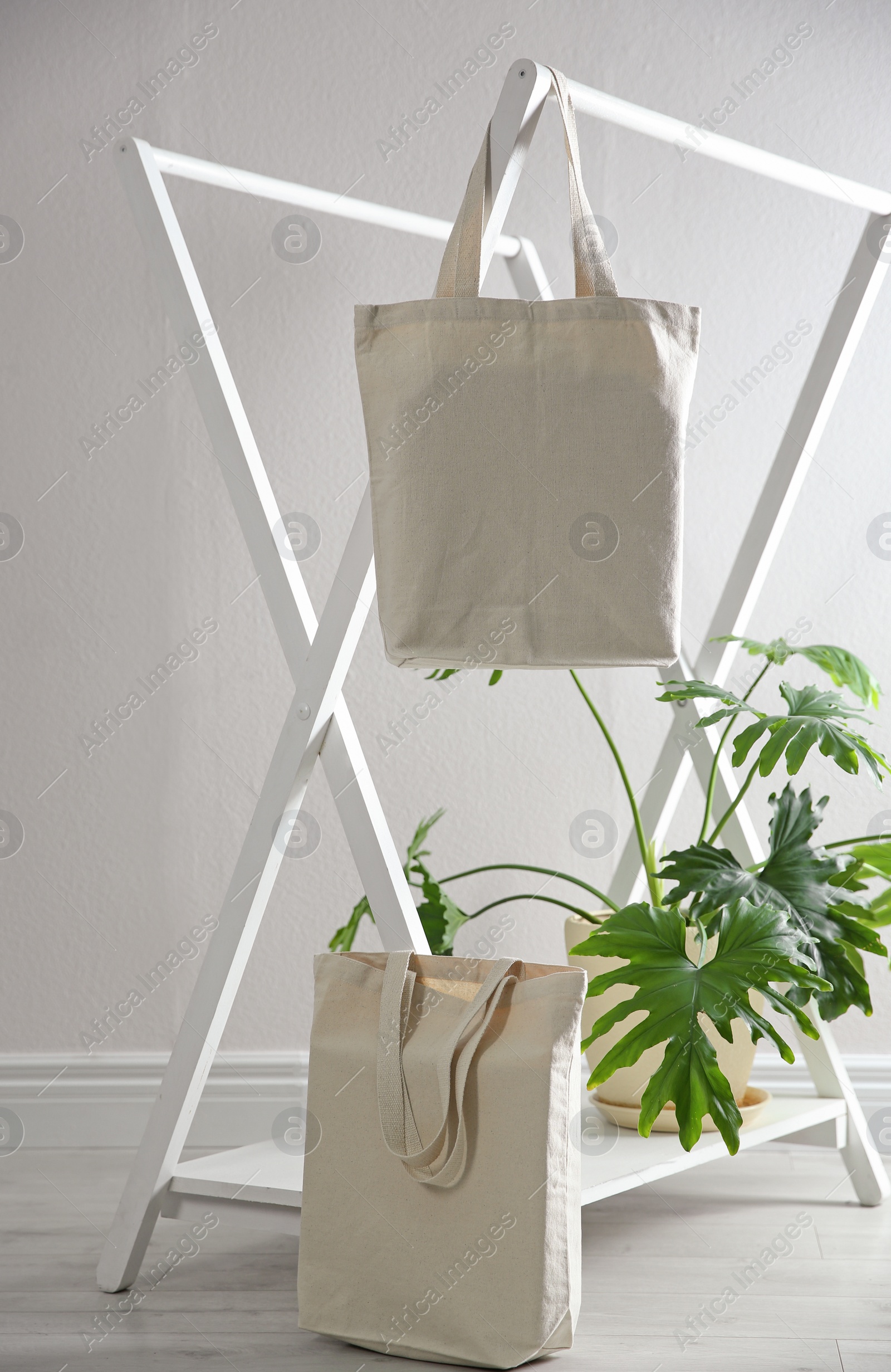 Photo of Eco bags with rack and houseplant near white wall. Space for design