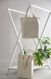 Photo of Eco bags with rack and houseplant near white wall. Space for design