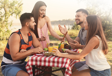 Image of Happy young people having picnic at table in park