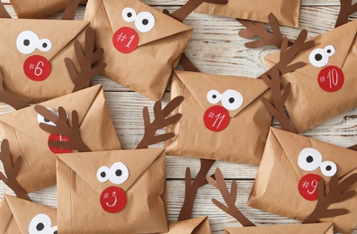 Photo of Set of gifts in envelopes with deer faces on white wooden table, flat lay. Christmas advent calendar