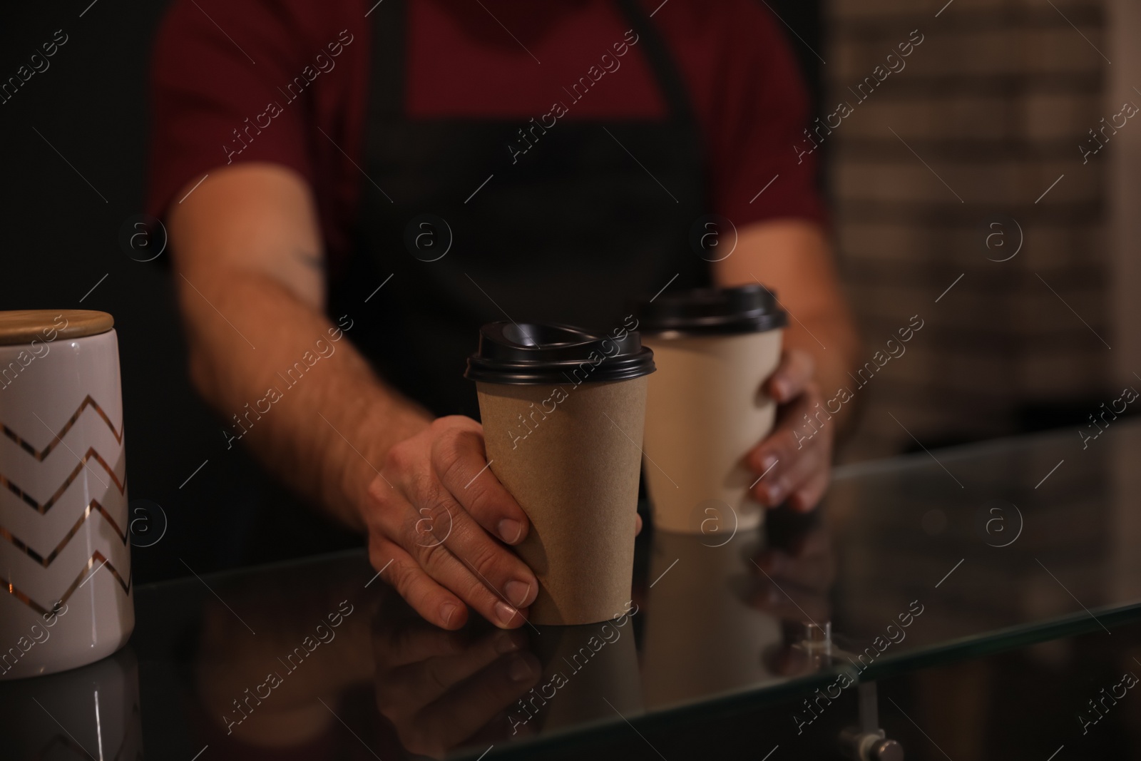 Photo of Barista putting takeaway coffee cups on glass table indoors, closeup