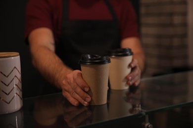 Photo of Barista putting takeaway coffee cups on glass table indoors, closeup