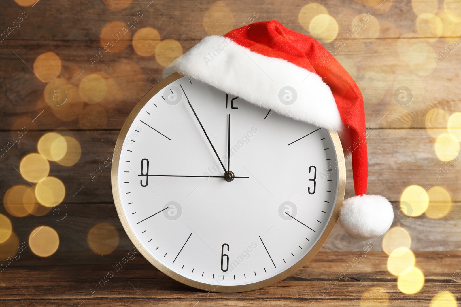 Photo of Clock with Santa hat showing five minutes until midnight on wooden background. New Year countdown