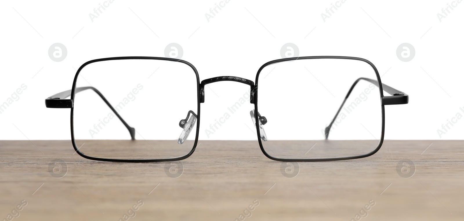 Photo of Stylish glasses with metal frame on wooden table against white background