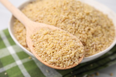 Photo of Bowl and spoon with raw bulgur on table, closeup
