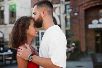 Photo of Handsome young man kissing his beautiful girlfriend on city street