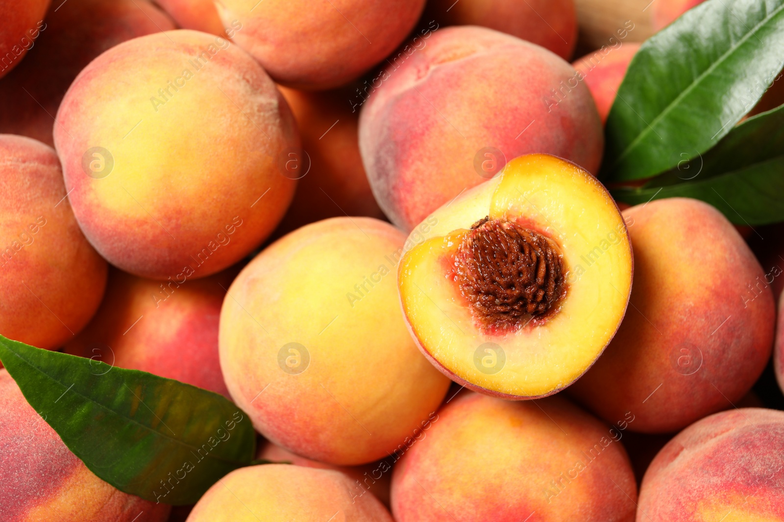 Photo of Cut and whole fresh ripe peaches with green leaves as background, top view