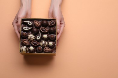 Photo of Woman with box of delicious chocolate candies on beige background, top view. Space for text