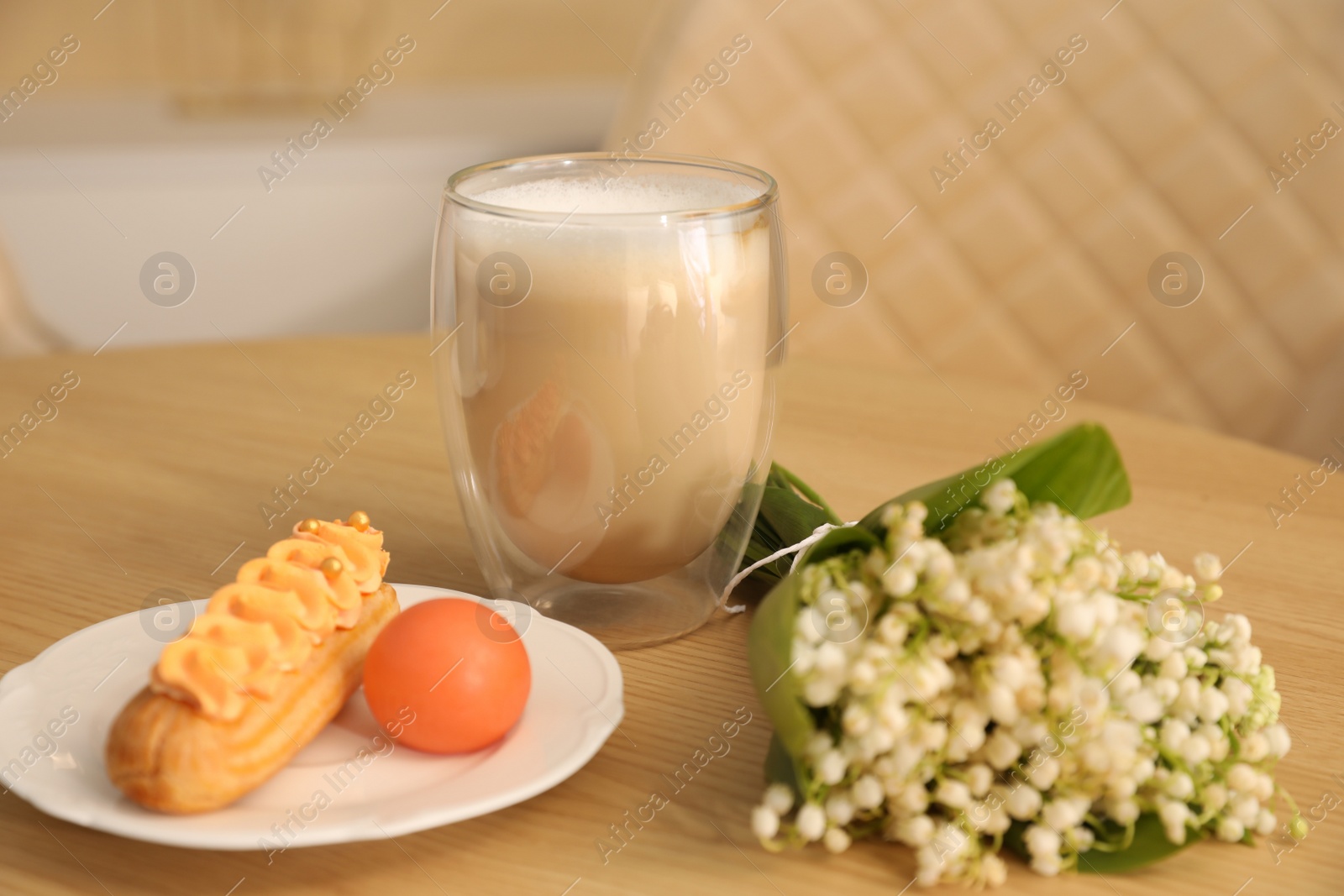 Photo of Cup of aromatic morning coffee, dessert and flowers on wooden table in cafe