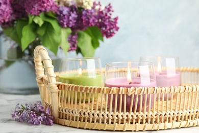 Photo of Tray with burning candles near lilac flowers on table