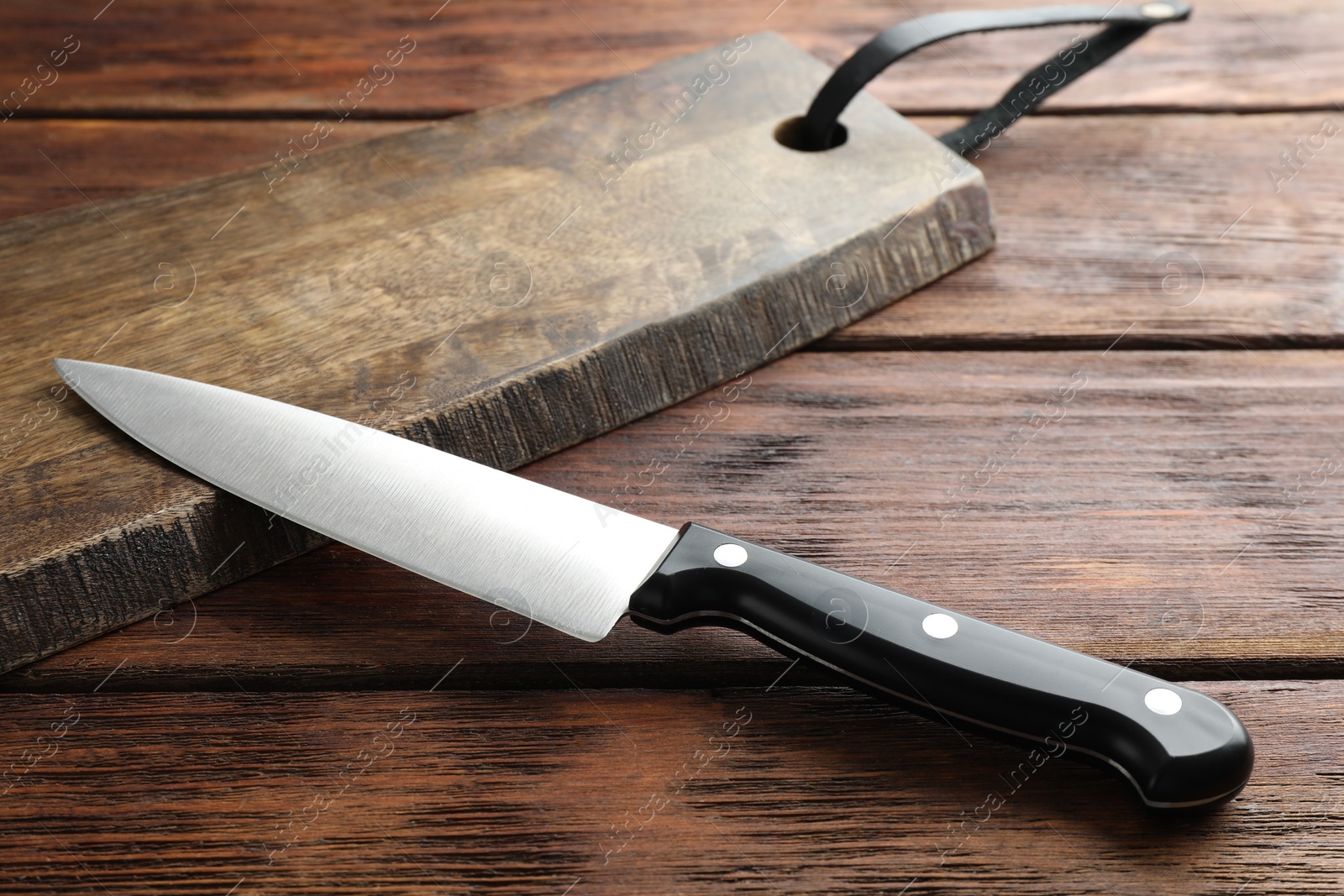 Photo of One sharp knife and board on wooden table, closeup