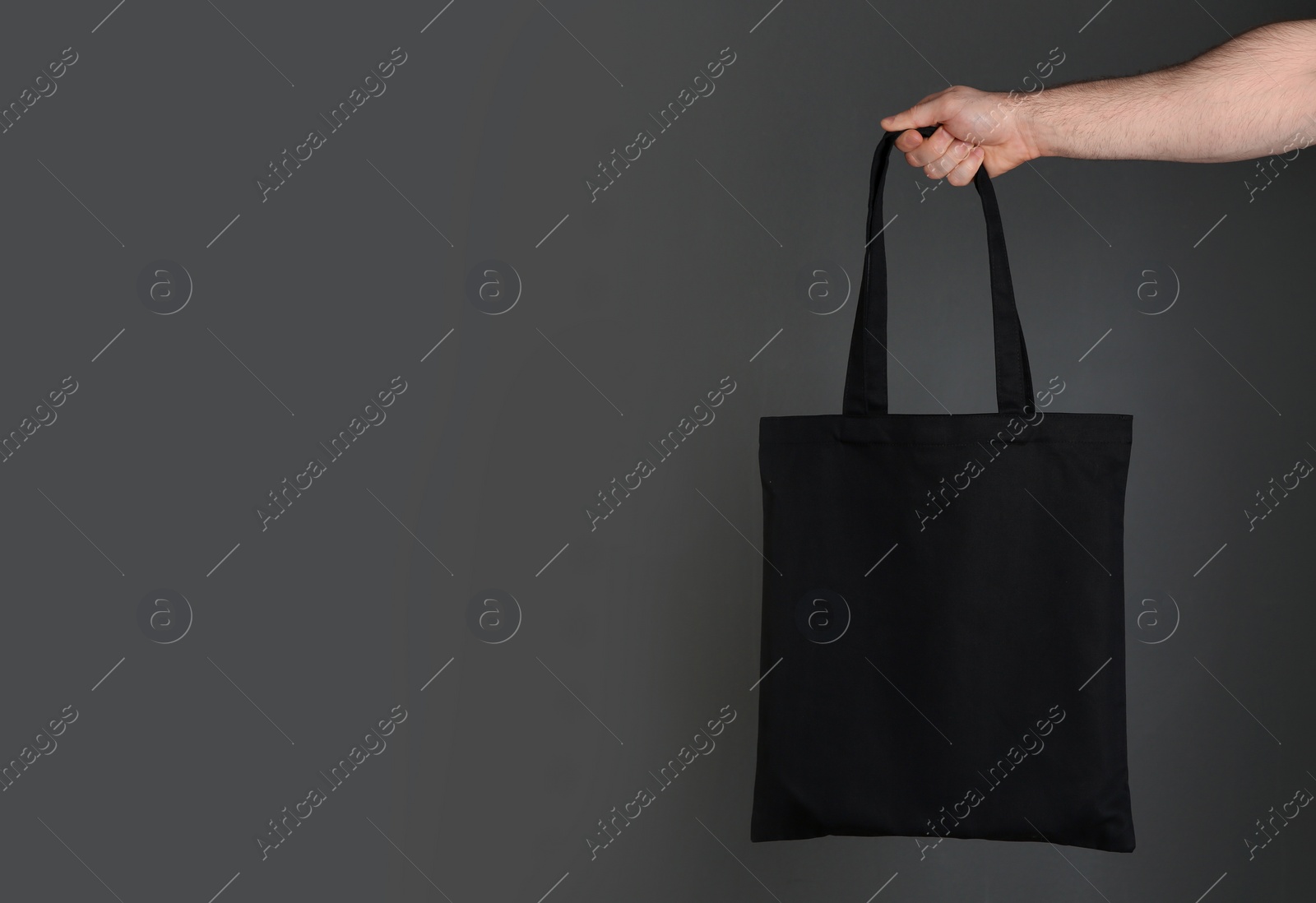 Photo of Man holding cotton shopping eco bag on grey background. Mockup for design