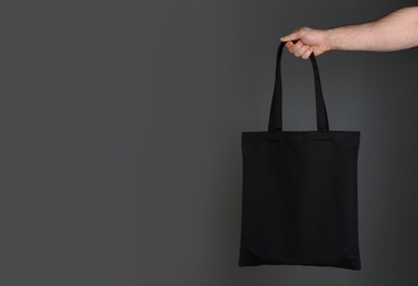 Photo of Man holding cotton shopping eco bag on grey background. Mockup for design