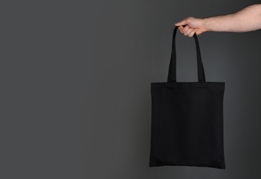 Man holding cotton shopping eco bag on grey background. Mockup for design