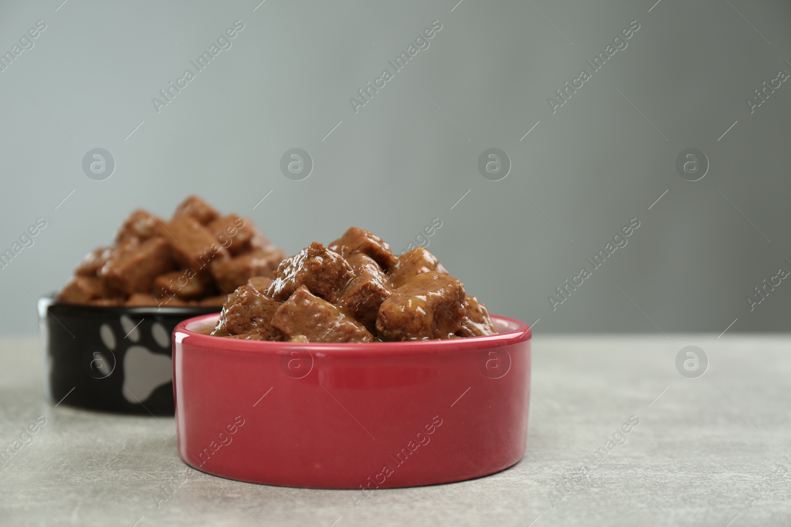 Photo of Wet pet food in feeding bowls on light grey table, space for text