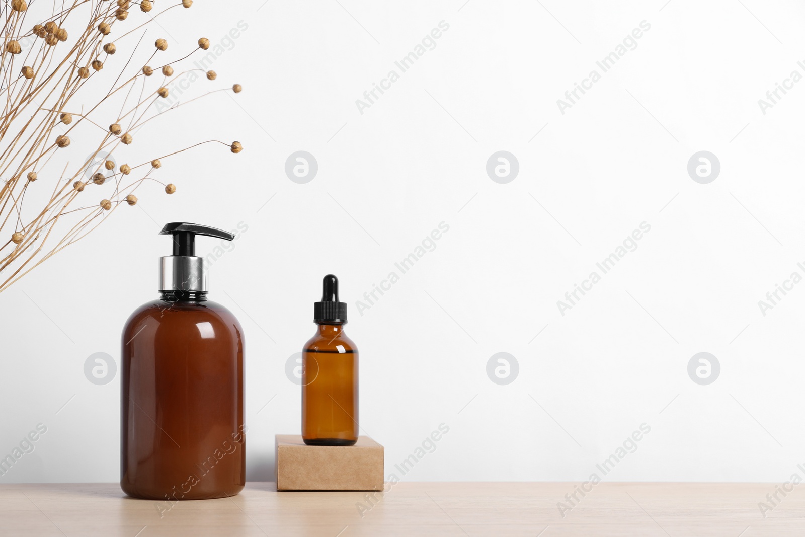 Photo of Bottles of cosmetic products and dry spikes on wooden table. Space for text
